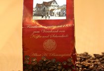 Eine Tüte steht in losen Kaffeebohnen. Auf der Tüte ist der Schriftzug "SchillerGarten. Kaffee. Familienkonzession seit 1880 zum Verschank von Kaffee und Schokolade" zu sehen.
