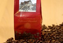 Eine Tüte steht in losen Kaffeebohnen. Auf der Tüte ist der Schriftzug "SchillerGarten. Espresso. Familienkonzession seit 1880 zum Verschank von Kaffee und Schokolade" zu sehen.