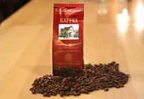 Eine Tüte steht in losen Kaffeebohnen. Auf der Tüte ist der Schriftzug "SchillerGarten. Kaffee. Familienkonzession seit 1880 zum Verschank von Kaffee und Schokolade" zu sehen.